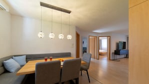 A modern dining area with a wooden table, grey upholstered seating, and hanging pendant lights.
