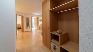 A hallway with wooden flooring, a wooden wardrobe with a hat on top, and a plant in the corner.