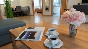 A wooden table with a magazine, two white cups of coffee, and a vase of flowers.