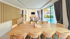 Una habitación de hotel moderna con zona de comedor, un conjunto de sofás y vistas a una piscina.