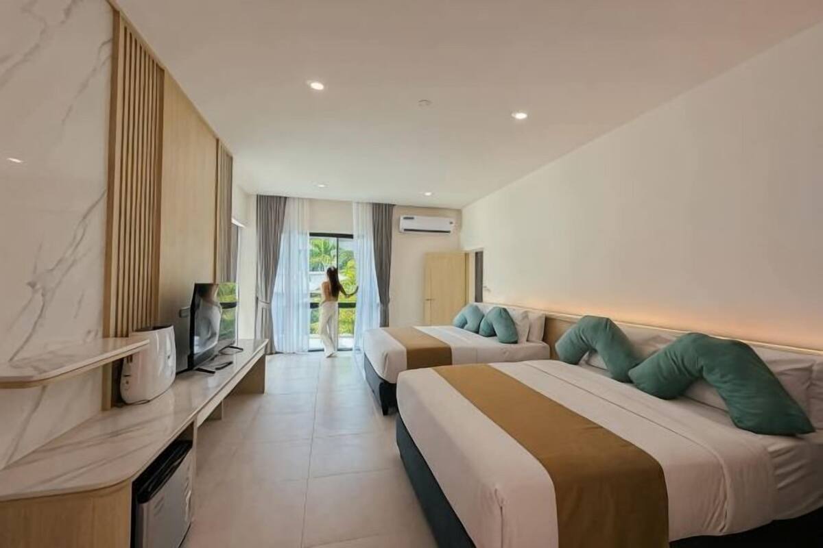 A hotel room with two beds, a TV, a desk, and a view of greenery outside.