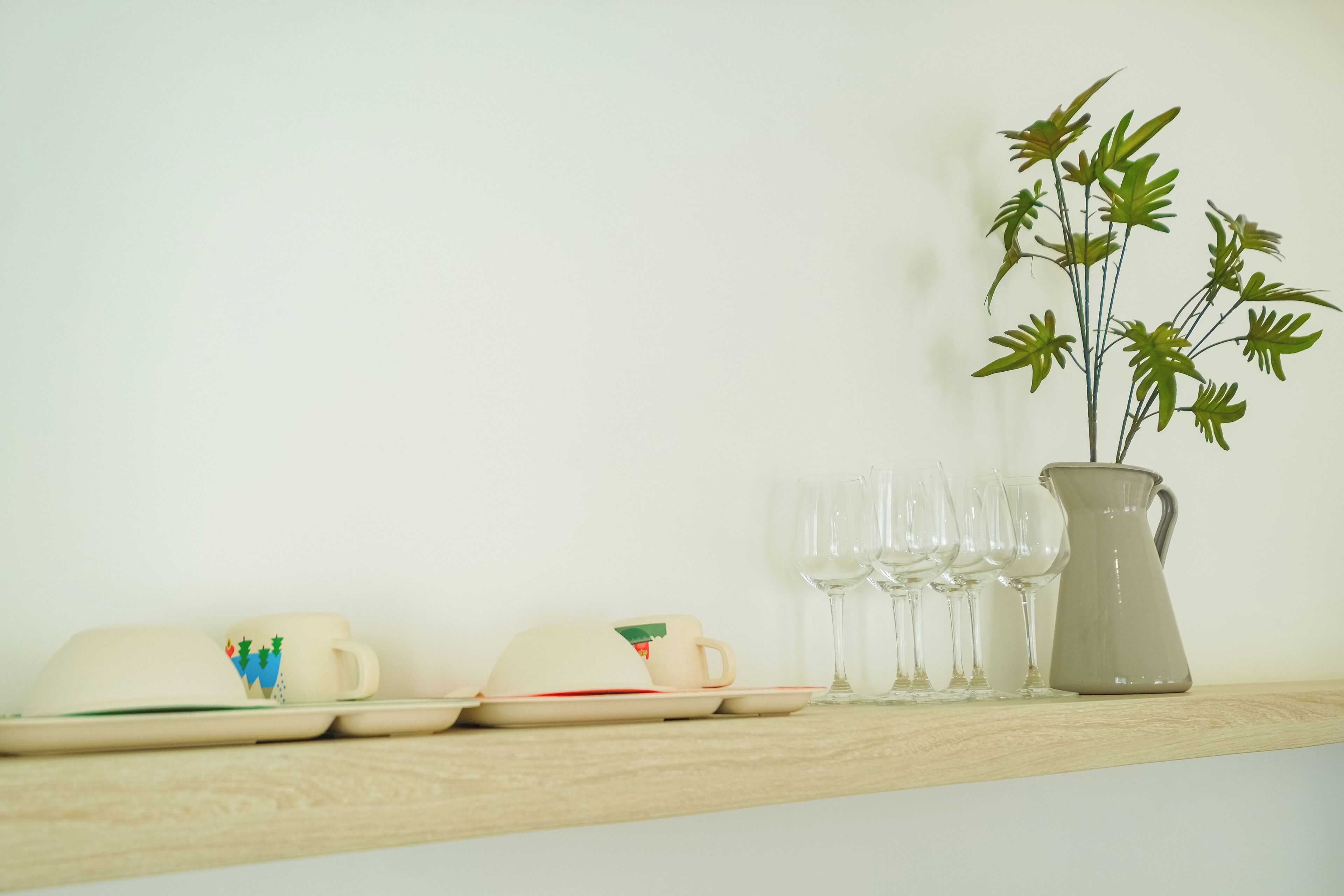 A wooden shelf with a ceramic pitcher, a ceramic mug, and several wine glasses.