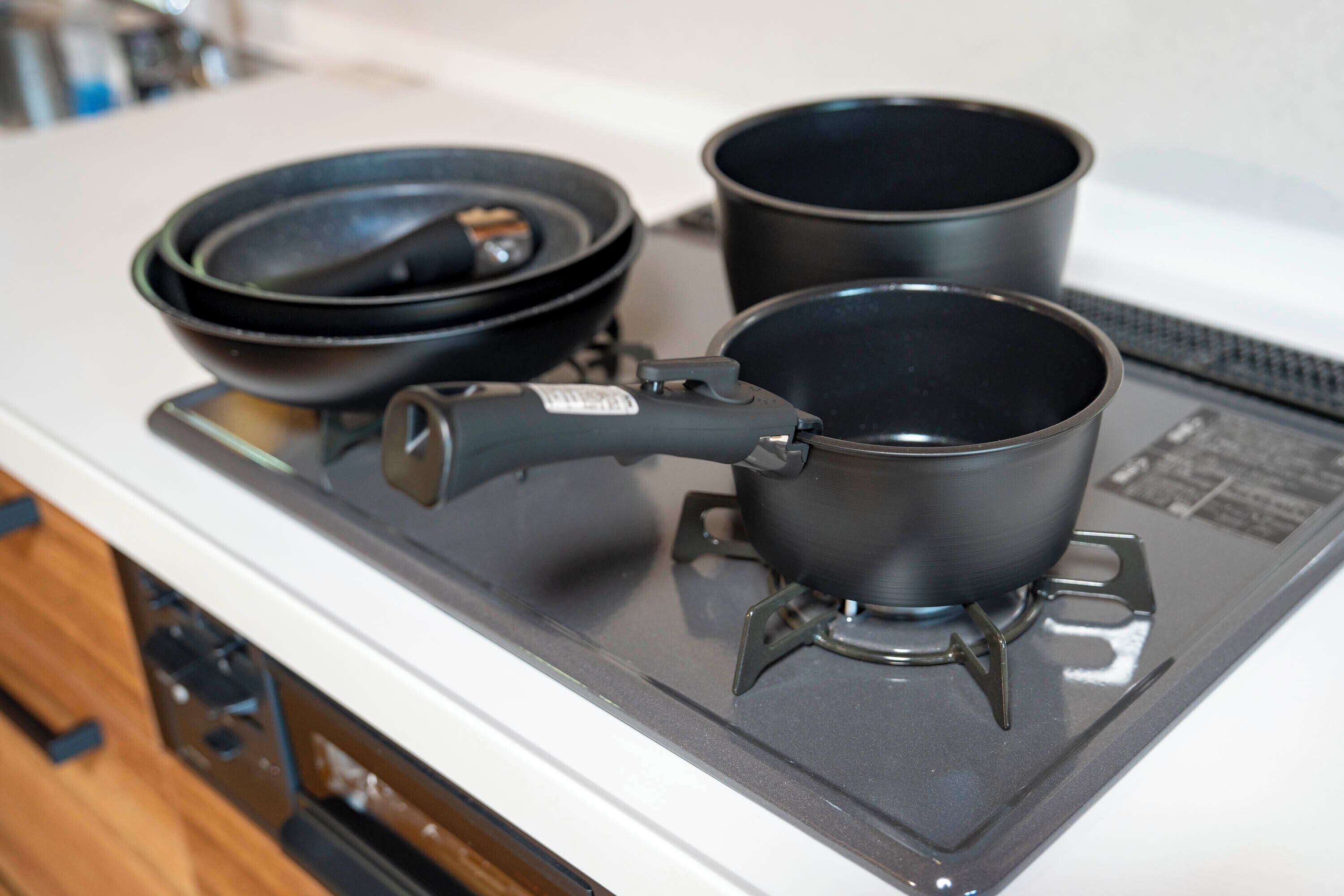 Un réchaud portatif avec deux casseroles et une poêle, posé sur un plan de travail blanc.