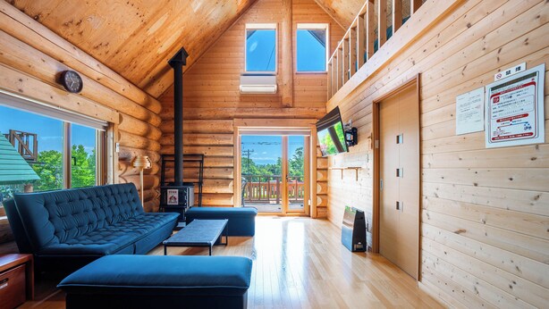 A log cabin interior with a sofa, ottoman, and a television on the wall. - LAKE TOYA MOON HILLS (Toyako)