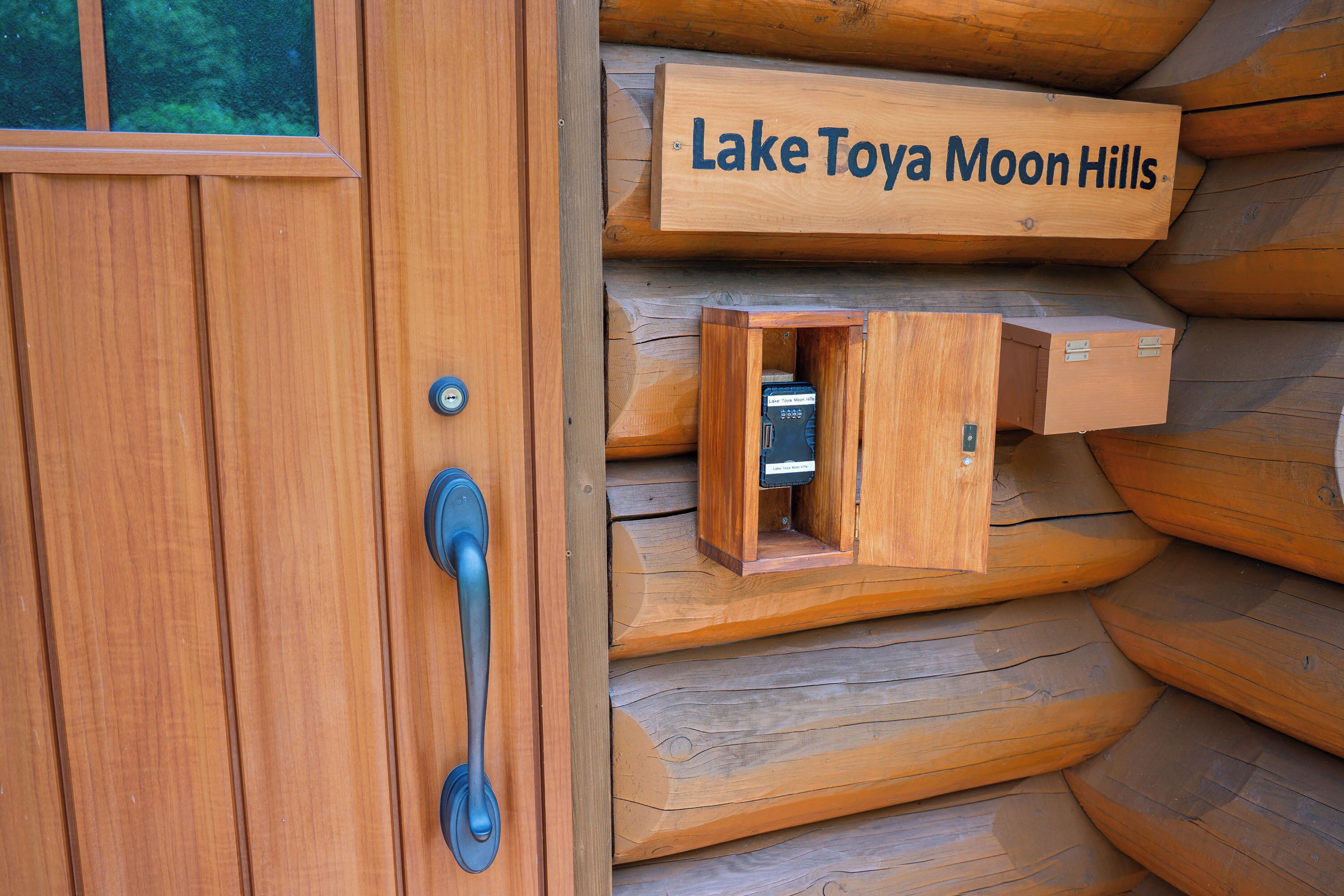 A wooden door with a sign reading 'Lake Tova Moon Hills' and a small wooden box with a key.