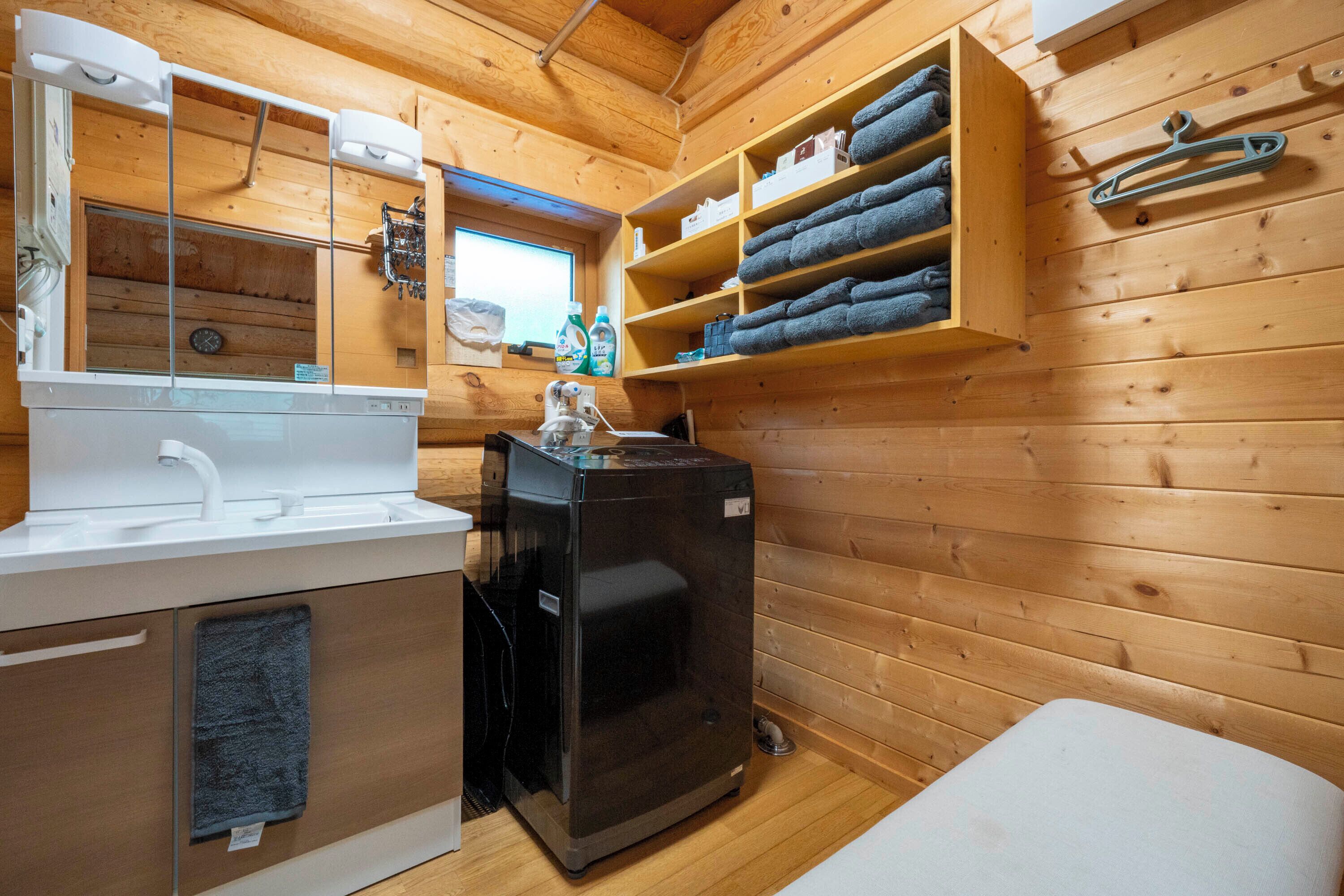 A compact wooden cabin with a white sink, a black heater, and shelves with folded towels.