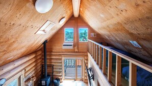 A log cabin interior with a wooden ceiling, a central chimney, and a view through a door to the outside. - LAKE TOYA MOON HILLS (Toyako)