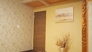 Ein Zimmer mit Holztür, einem an der Wand befestigten abstrakten Gemälde und einer Vase mit Trockenpflanzen.
