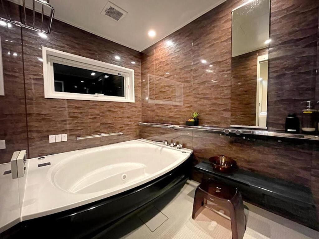 A modern bathroom with a large bathtub, a vanity with a mirror, and a small stool.