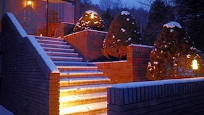 Ein modernes Gebäude mit einer Treppe, die zu einem Glastürbereich führt, umgeben von schneebedeckten Bäumen und Ziegelmauern.