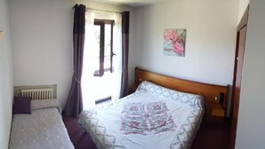A bedroom with a wooden bed, a radiator, a window with curtains, and a painting on the wall. - HOTEL LA GRANGE (Boutx)