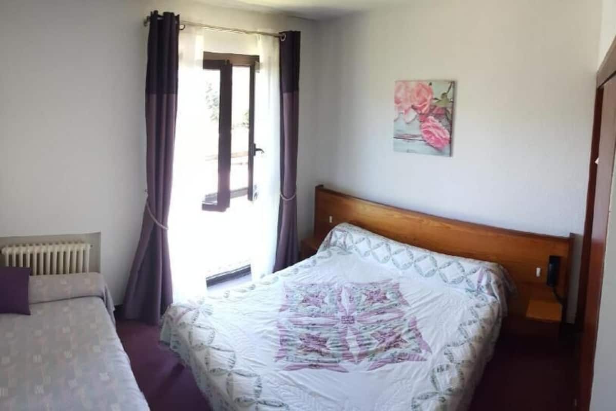 A bedroom with a wooden bed, a radiator, a window with curtains, and a painting on the wall.