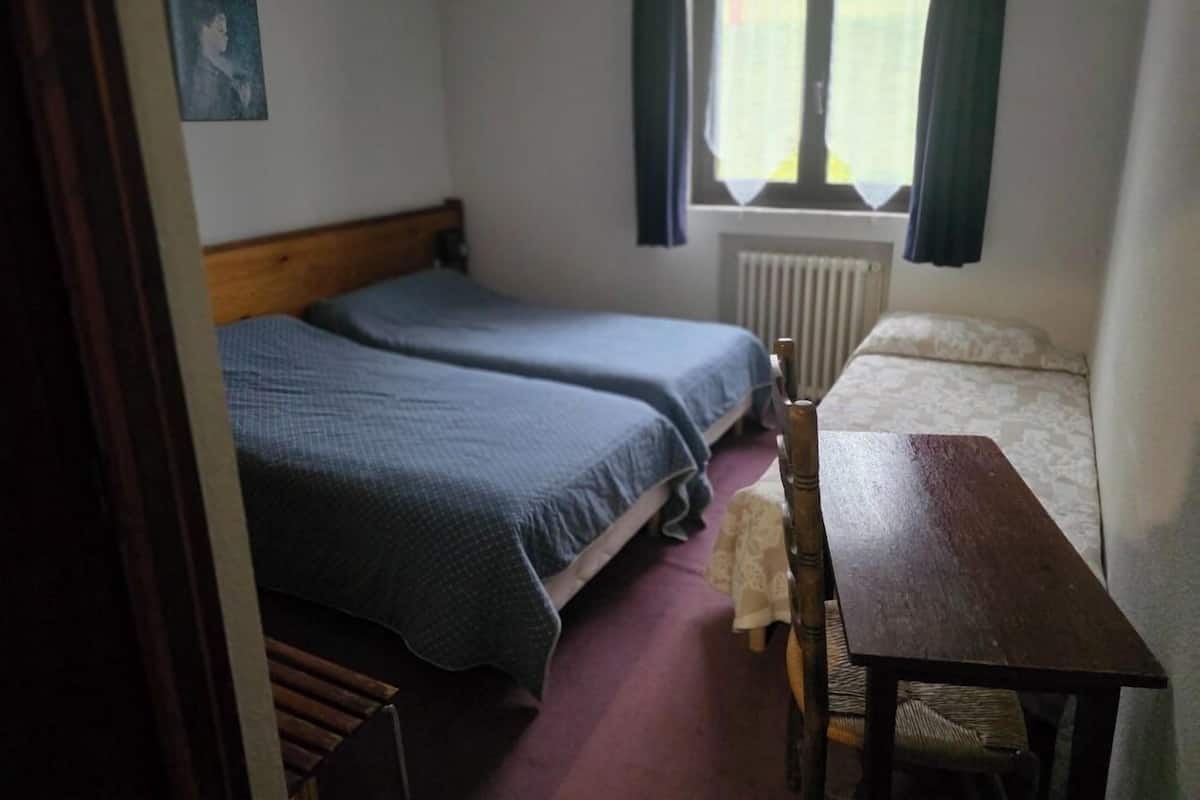 A room with two single beds, a wooden table, a bench, and a window with curtains.