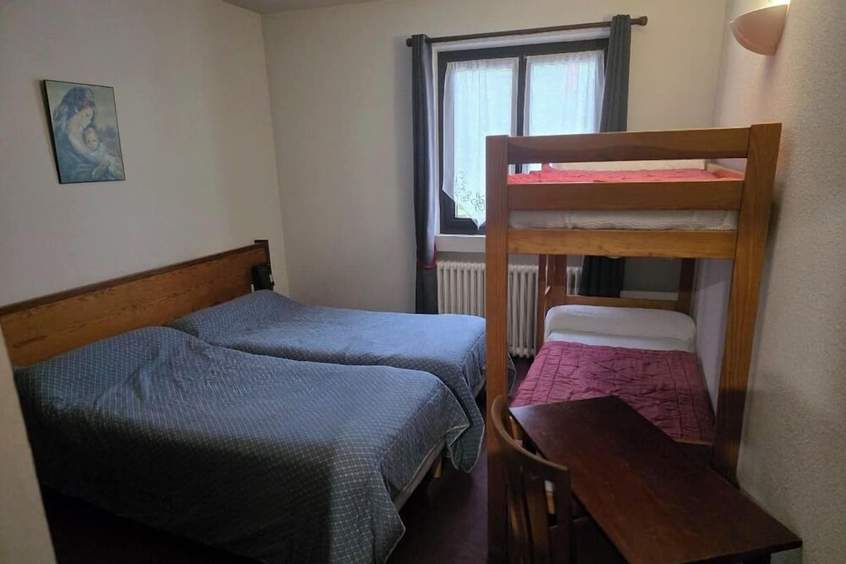 A small, cozy room with two single beds, a wooden desk, and a window with curtains.