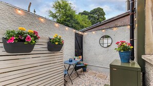 Un espace patio avec une table et des chaises en bois, des plantes en pot et un petit miroir rond accroché au mur.