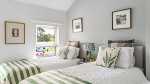 Une chambre avec deux lits, une fenêtre avec des stores et des tableaux encadrés accrochés au mur.