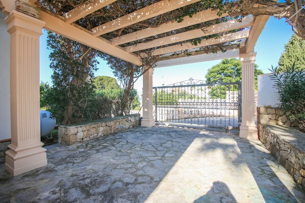 A covered outdoor area with stone flooring, columns, and a pergola with vines.