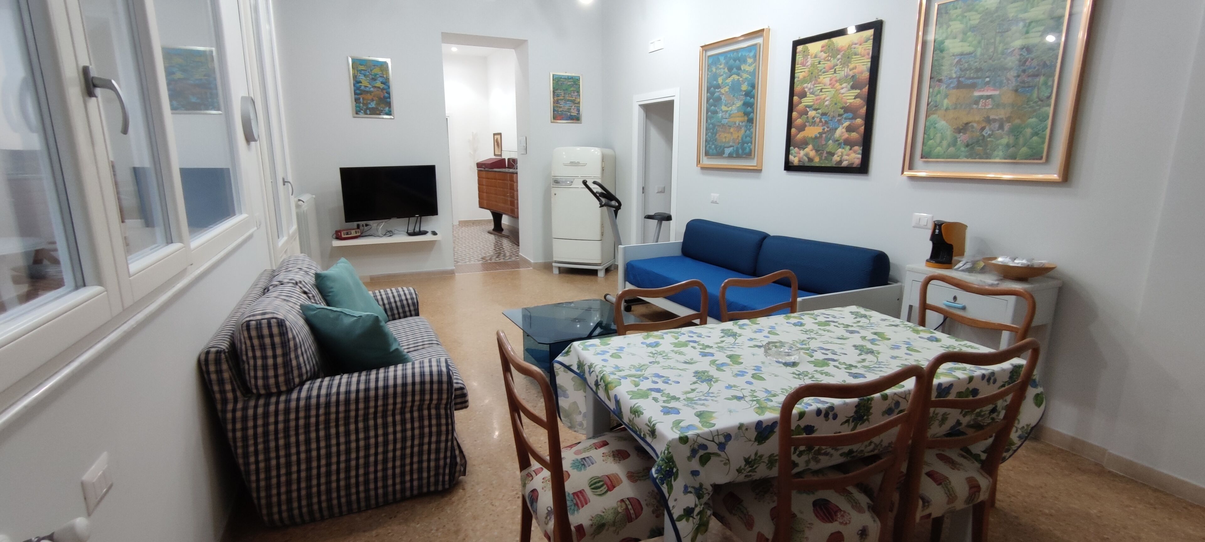 Ein gemütlicher, kompakter Wohnraum mit Sofa, Esstisch mit Stühlen, Fernseher, Kühlschrank und Wandbildern.