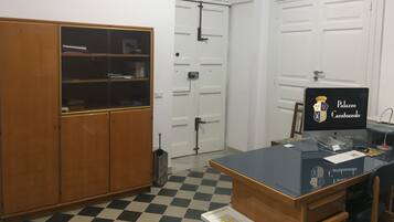A room with a checkered floor, a wooden cabinet, a desk with a computer, and a door with a decorative arch.
