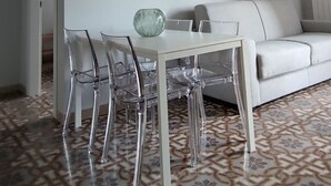 A dining area with a white table and chairs, a patterned floor, and a white sofa. - Palazzo Caratozzolo (Agrigento)