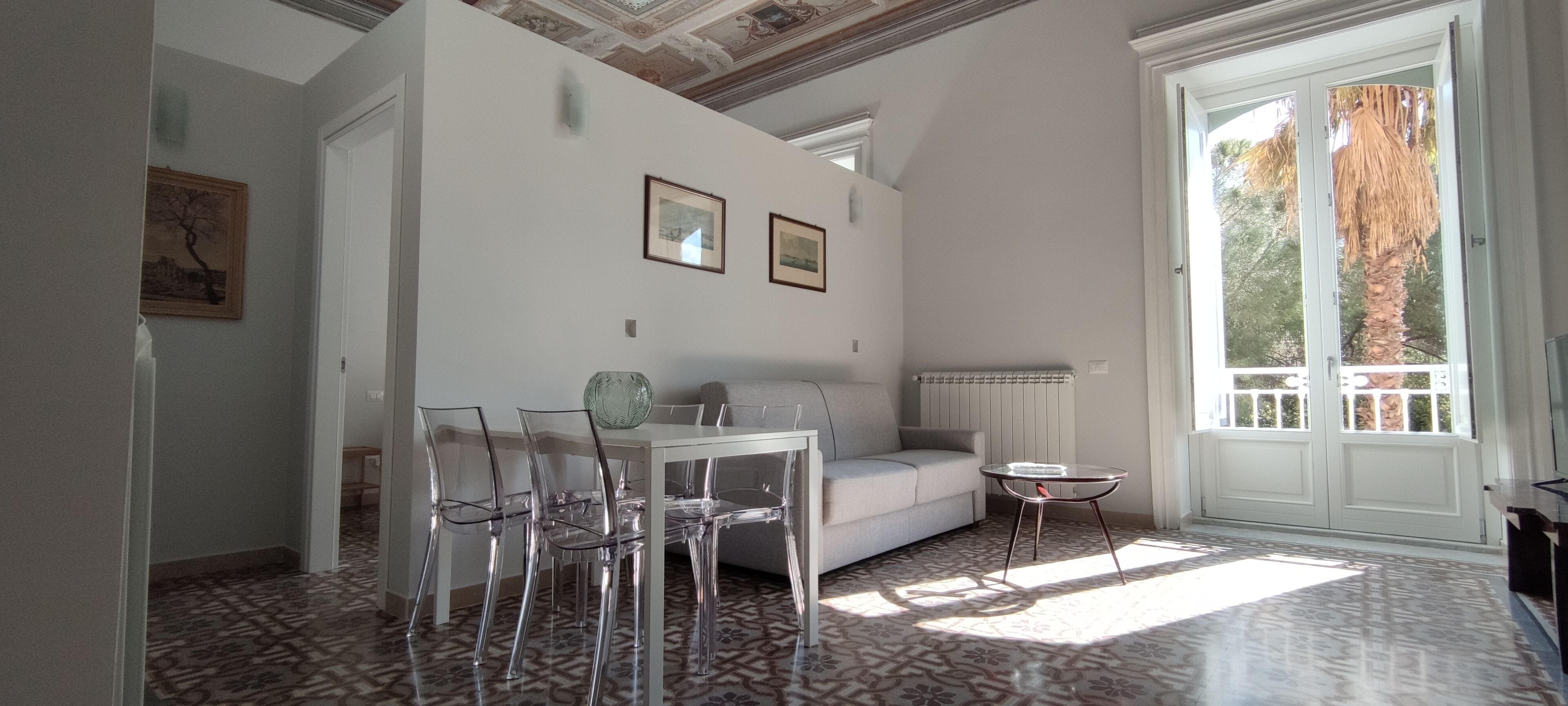 Een kamer met een witte bank, transparante stoelen, een klein tafeltje en een vloer met een patroon.