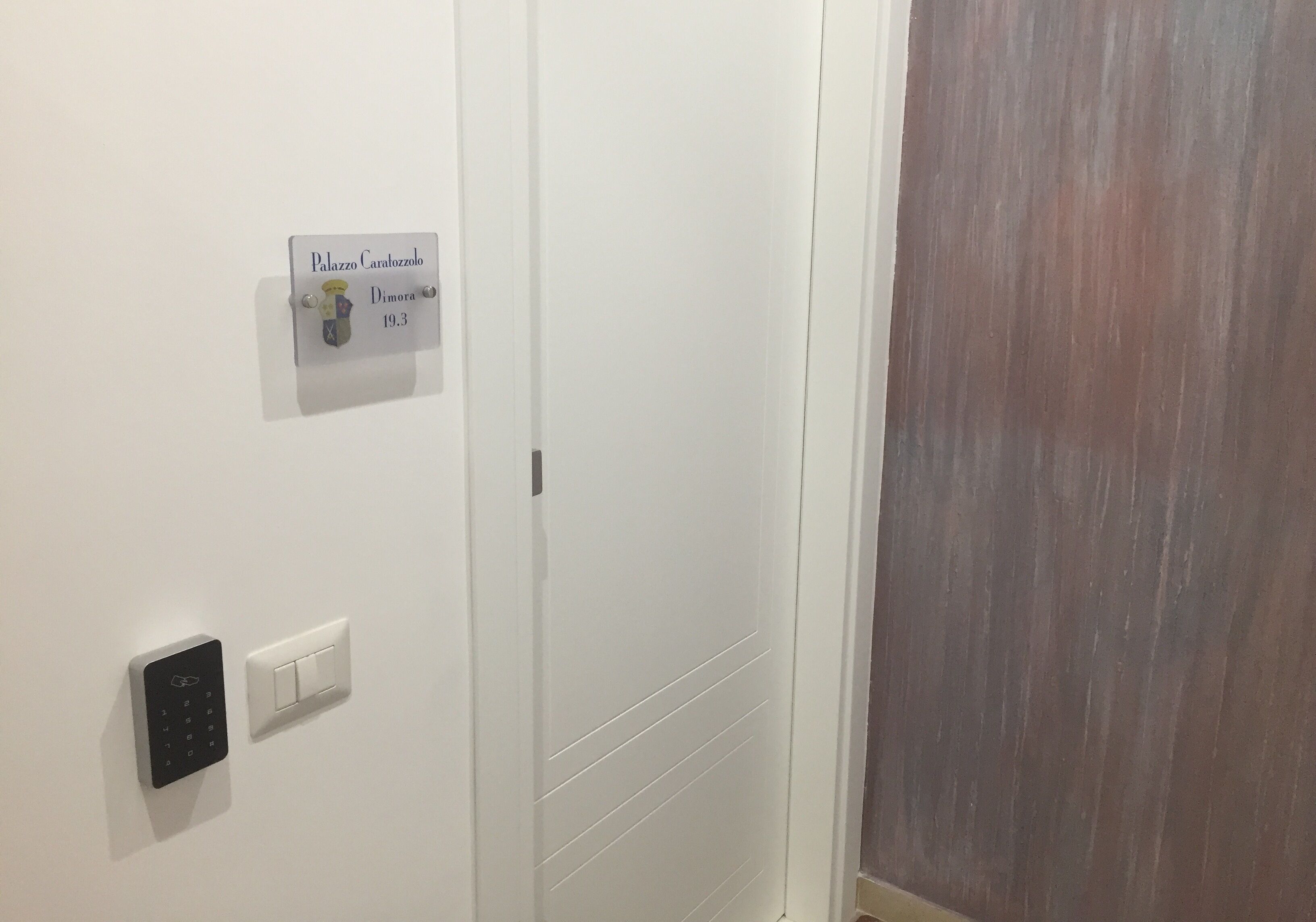 A door with a sign reading "Palazzo Carrozzo 19.3" and a wall-mounted light switch.