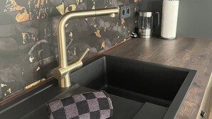Una cocina con encimera negra, grifo dorado, toalla de cuadros y cafetera.