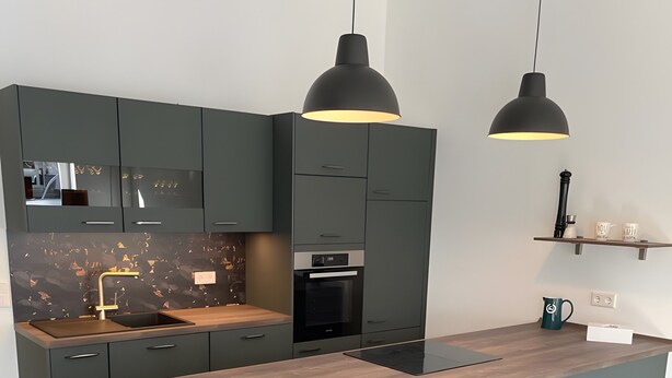 Una cocina moderna con armarios oscuros, una isla central, iluminación colgante y electrodomésticos integrados.