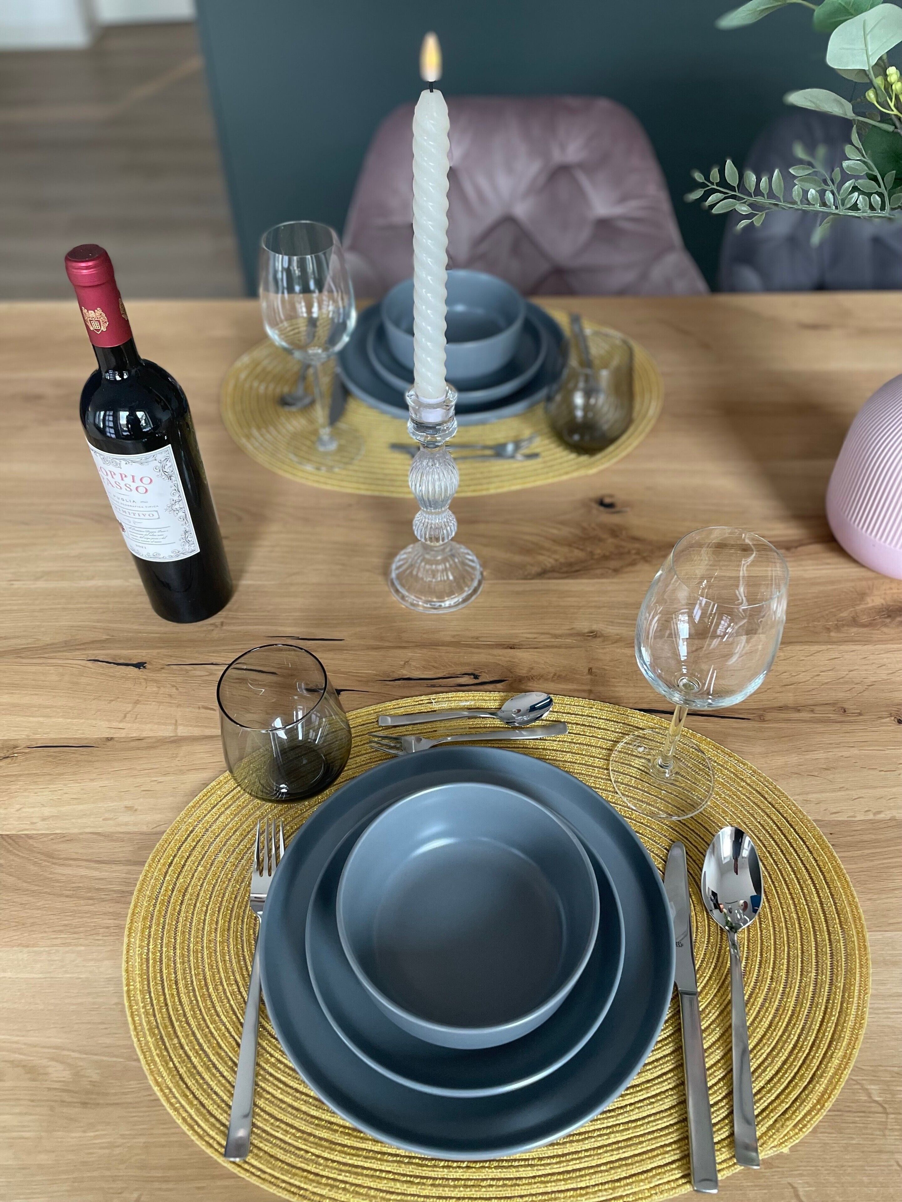 A dining table set with plates, cutlery, a candle, and a wine bottle.
