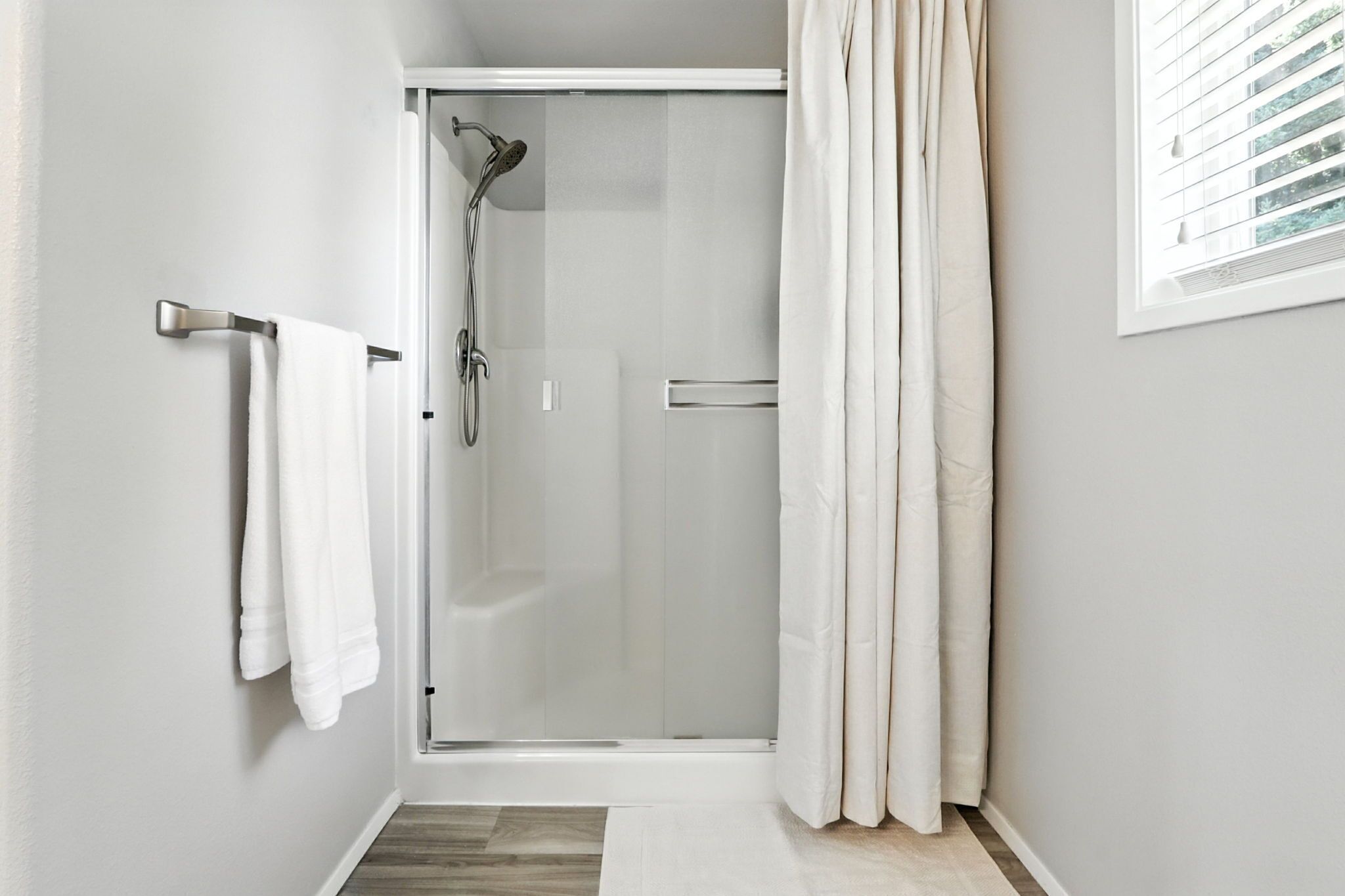 Un baño moderno con cabina de ducha de vidrio, un perchero y una ventana con persianas.