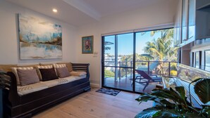 A modern living room with a dark brown sofa, a large abstract painting, and a view of palm trees through a sliding glass door. - Roomy Duplex with water views. Steps  away from Castle Rock Beach (Clontarf)