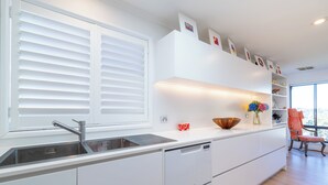 A modern kitchen with white cabinetry, a built-in dishwasher, and a large window with blinds. - Roomy Duplex with water views. Steps  away from Castle Rock Beach (Clontarf)