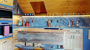 A kitchen with wooden cabinets, a marble backsplash, and a wooden island with stools. - Downtown Boothbay Harbor Studio – Ocean Views, Dog-Friendly, Walk to Pier (Boothbay Harbor)