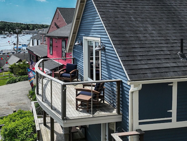 Une maison dotée d’un balcon avec deux chaises et une table, donnant sur une marina où sont amarrés des bateaux.