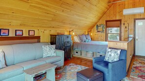 A cozy cabin interior with a loft bed, a sofa, a small table, and a cabinet. - Downtown Boothbay Harbor Studio – Ocean Views, Dog-Friendly, Walk to Pier (Boothbay Harbor)