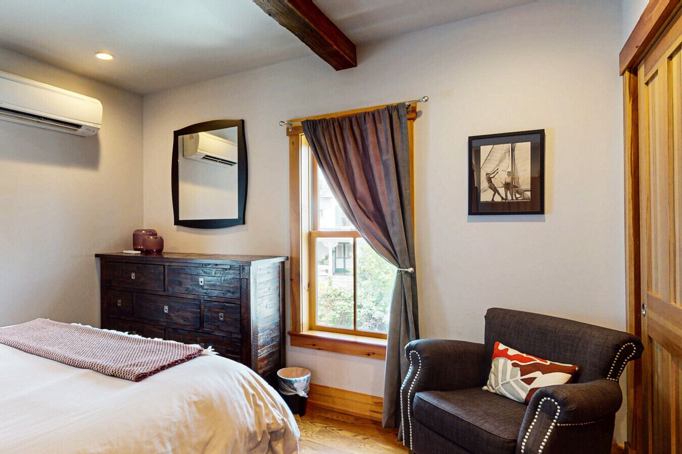 A bedroom with a bed, dresser, chair, and a window with curtains.