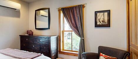 A bedroom with a bed, dresser, chair, and a window with curtains.