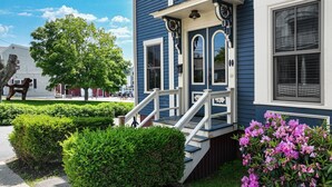 A two-story house with a front porch, a staircase, and a well-maintained garden with shrubs and flowers.