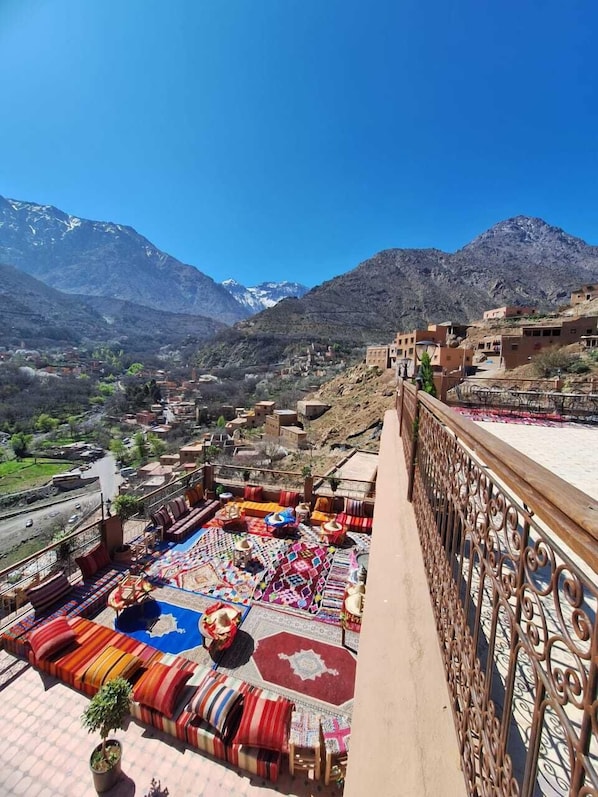Une terrasse sur le toit, agrémentée de tapis et de coussins aux couleurs vives, d’où l’on peut admirer un paysage montagneux.