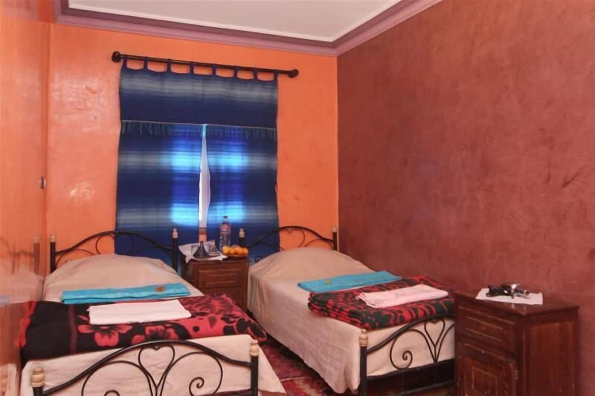 Une chambre avec deux lits, une table de chevet, une commode et une fenêtre avec un rideau.