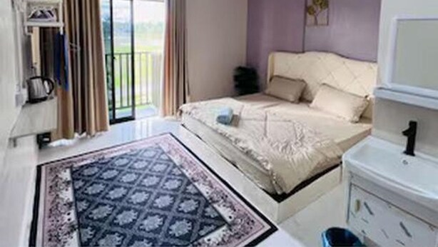 Un dormitorio con cama, una mesita de noche, televisor y ventana con cortinas.