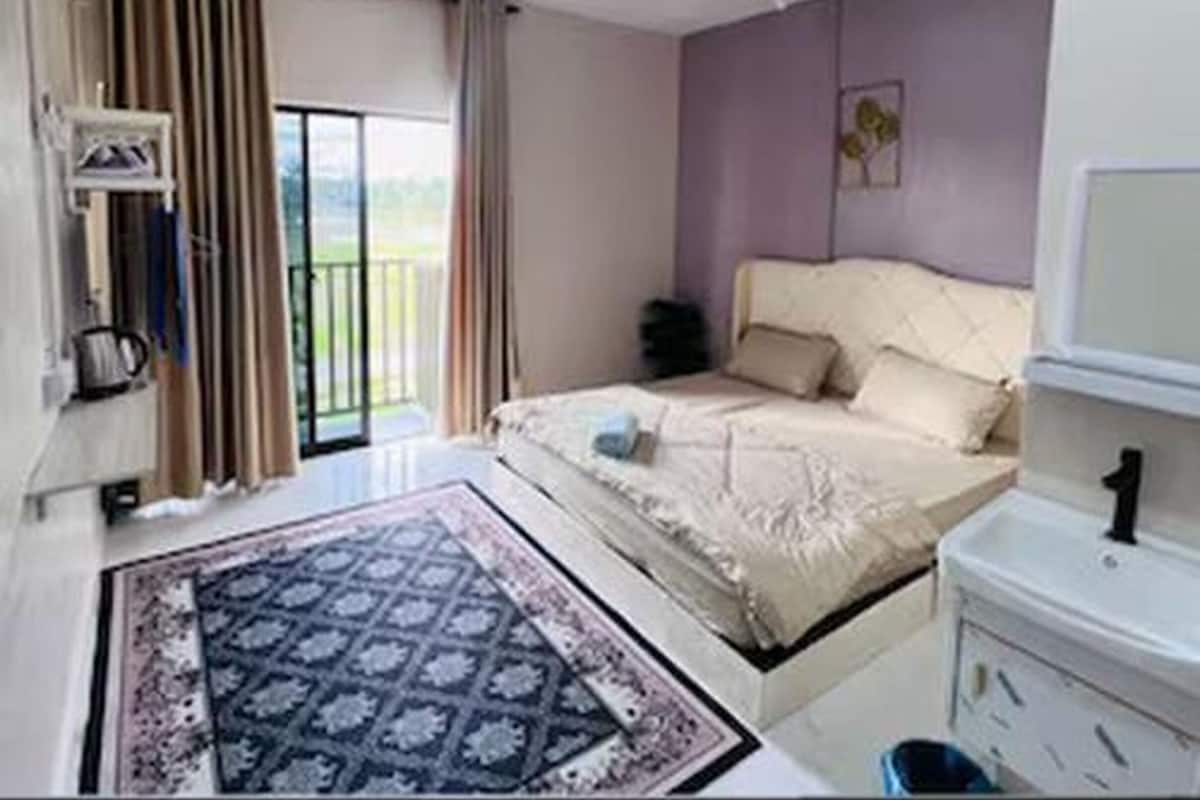 Une chambre à coucher avec un lit, une petite table de chevet, une télévision et une fenêtre avec des rideaux.