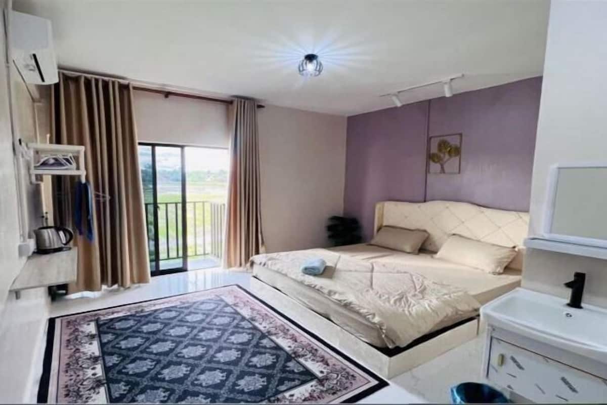 Une chambre à coucher comprenant un lit, une table de chevet, une fenêtre avec des rideaux, un luminaire au plafond et une vue sur l’extérieur.