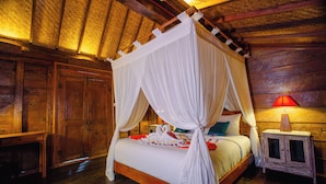 Una cama con dosel de madera con cortinas blancas, una mesita de noche con lámpara y un armario de madera.