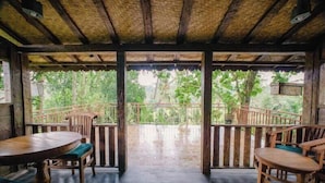Una terraza de madera con techo de paja, barandillas de madera y vista a vegetación exuberante.