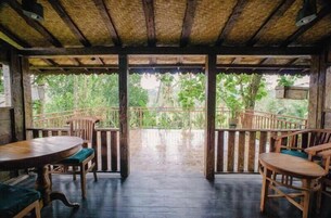 Una terraza de madera con techo de paja, barandillas de madera y vista a vegetación exuberante.