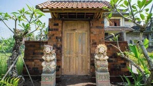 Una reja de madera tradicional con dos estatuas a cada lado, que da acceso a una edificación con techo de tejas.