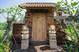 Una reja de madera tradicional con dos estatuas a cada lado, que da acceso a una edificación con techo de tejas.