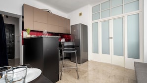 A modern kitchen with a built-in refrigerator, a dining area with a table and chairs, and a large window with frosted glass panels. - Apartamenty Sun & Snow Wałowa (Warsaw)