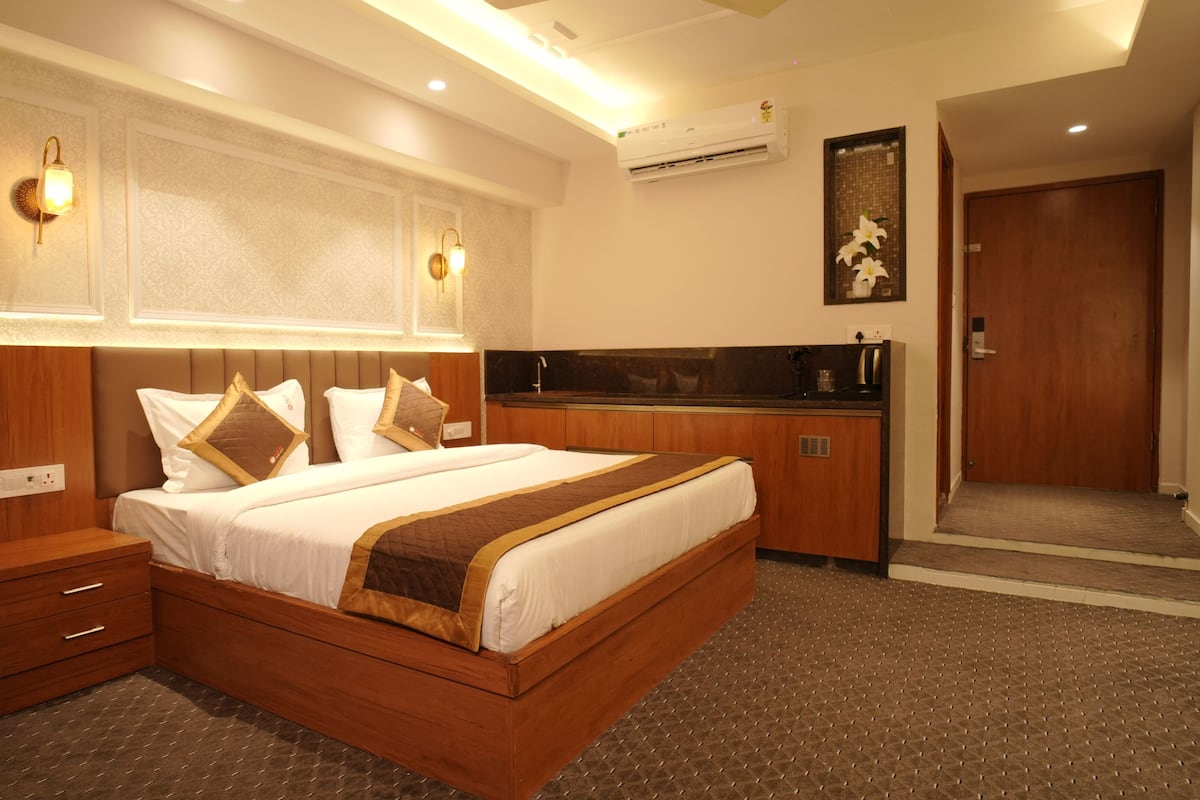 A hotel room with a wooden bed, bedside tables, a small kitchenette, and a door leading to another room.